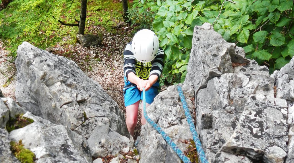 Junge mit Klettergurt wird abgeseilt durch Ablassen