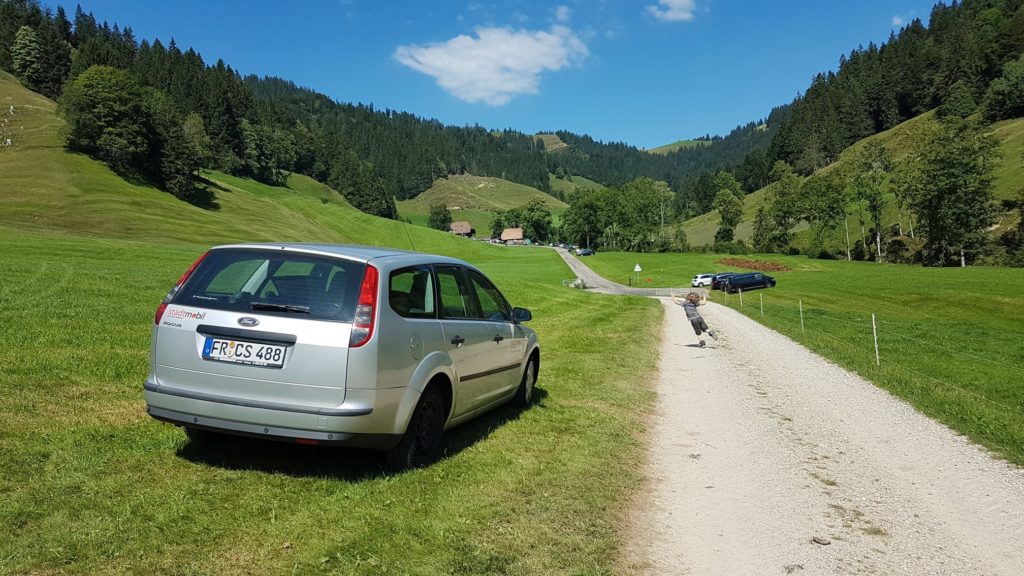 Auto auf der Wiese und tanzendes Kind