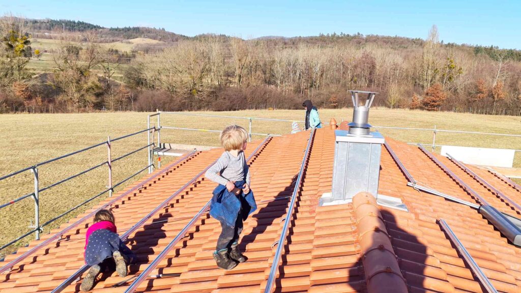 Kinder erforschen unser Hausdach, im Hintergrund Natur und Gleitschirmflieger