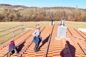 Kinder erforschen unser Hausdach, im Hintergrund Natur und Gleitschirmflieger