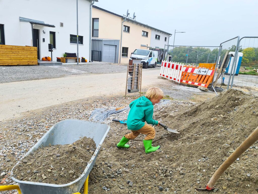 Ein Kind schippt einen Haufen Kies in eine Schubkarre